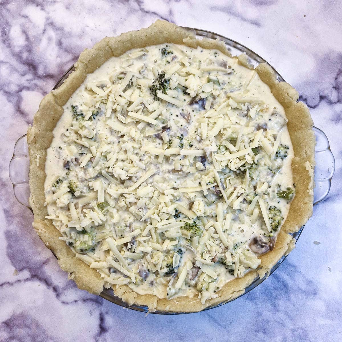 Broccoli quiche filling poured into a pastry shell in covered in grated cheese.