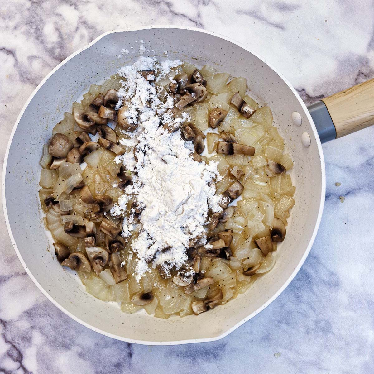 Flour sprinkled on mushrooms and onions in a frying pan.