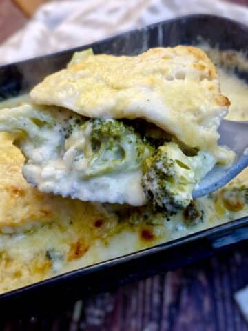 Close up of a slice of baked cod on a spoonful of broccoli, covered in cheese sauce.
