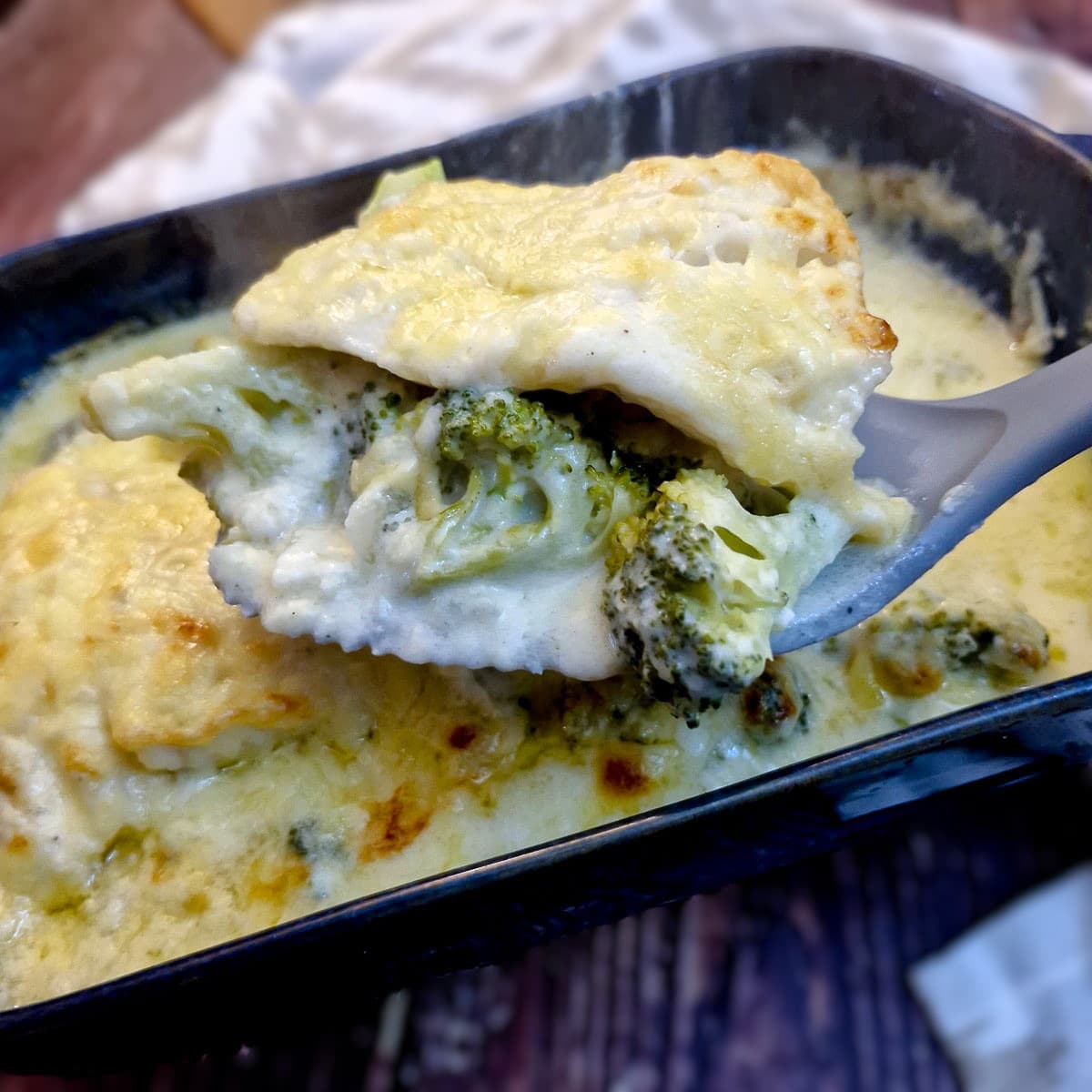 Close up of a slice of baked cod on a spoonful of broccoli, covered in cheese sauce.