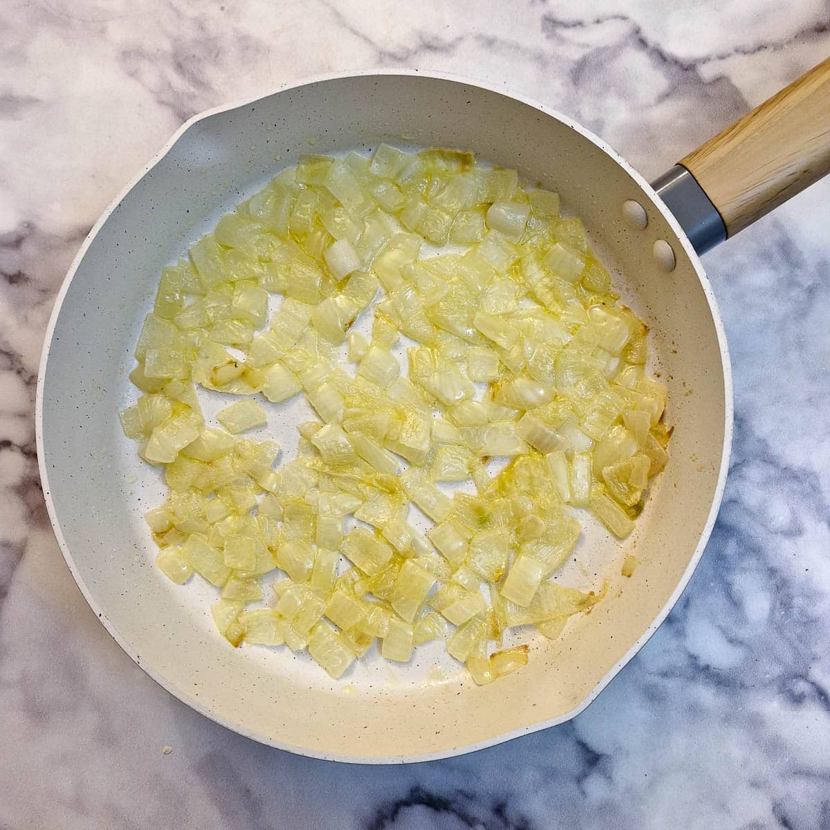 Onions frying in butter in a white frying pan.