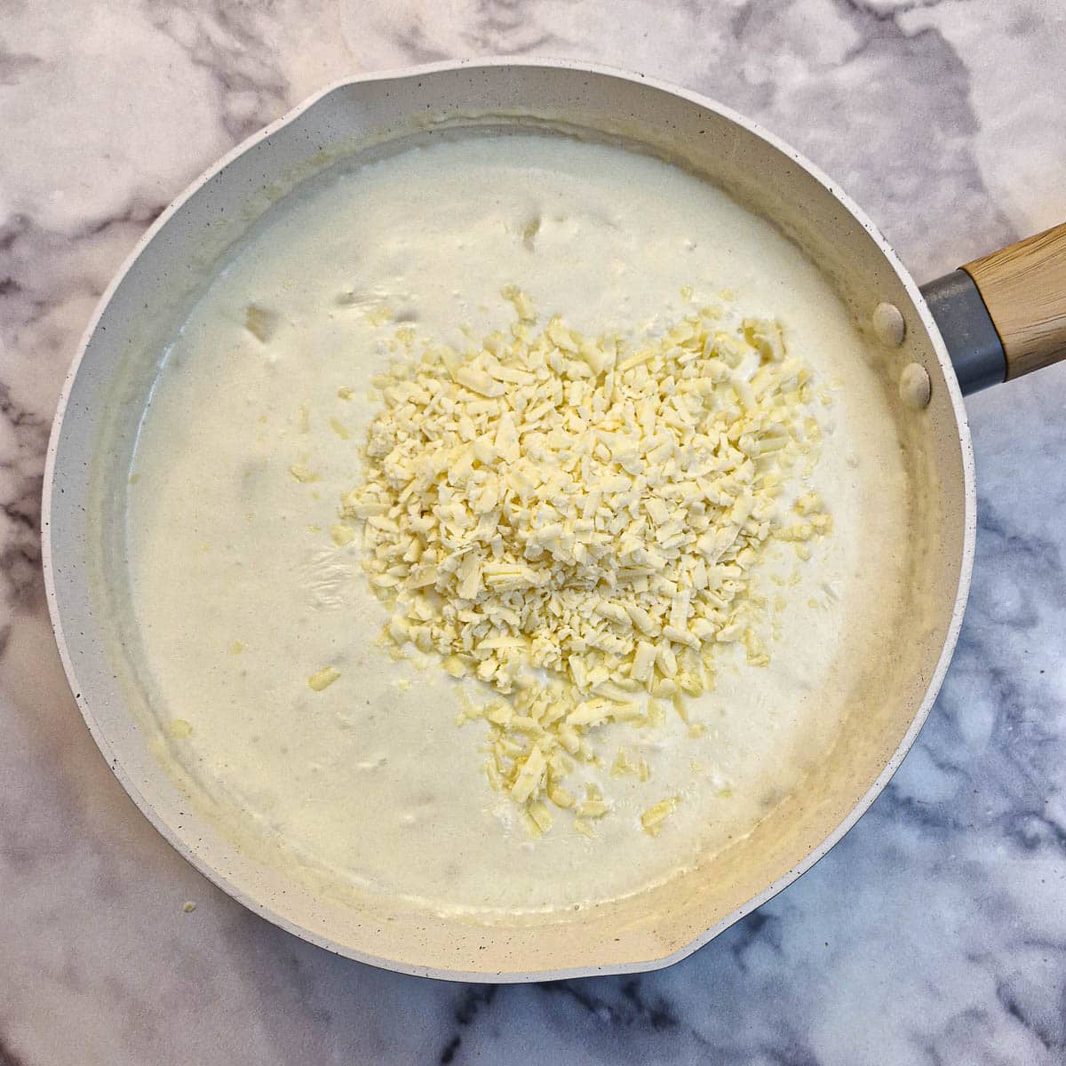 Grated cheese added to the sauce in a frying pan.