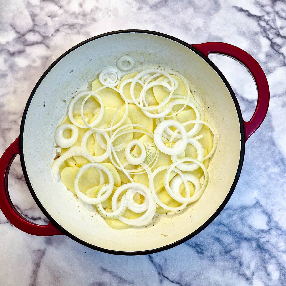 Sliced potatoes and onions being layered in a casserole dish.