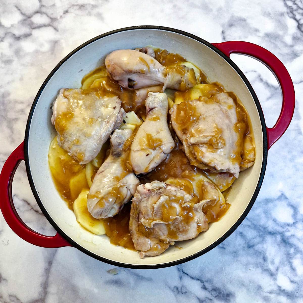 Chicken pieces covered in French onion soup on top of layers of potatoes in a casserole dish.