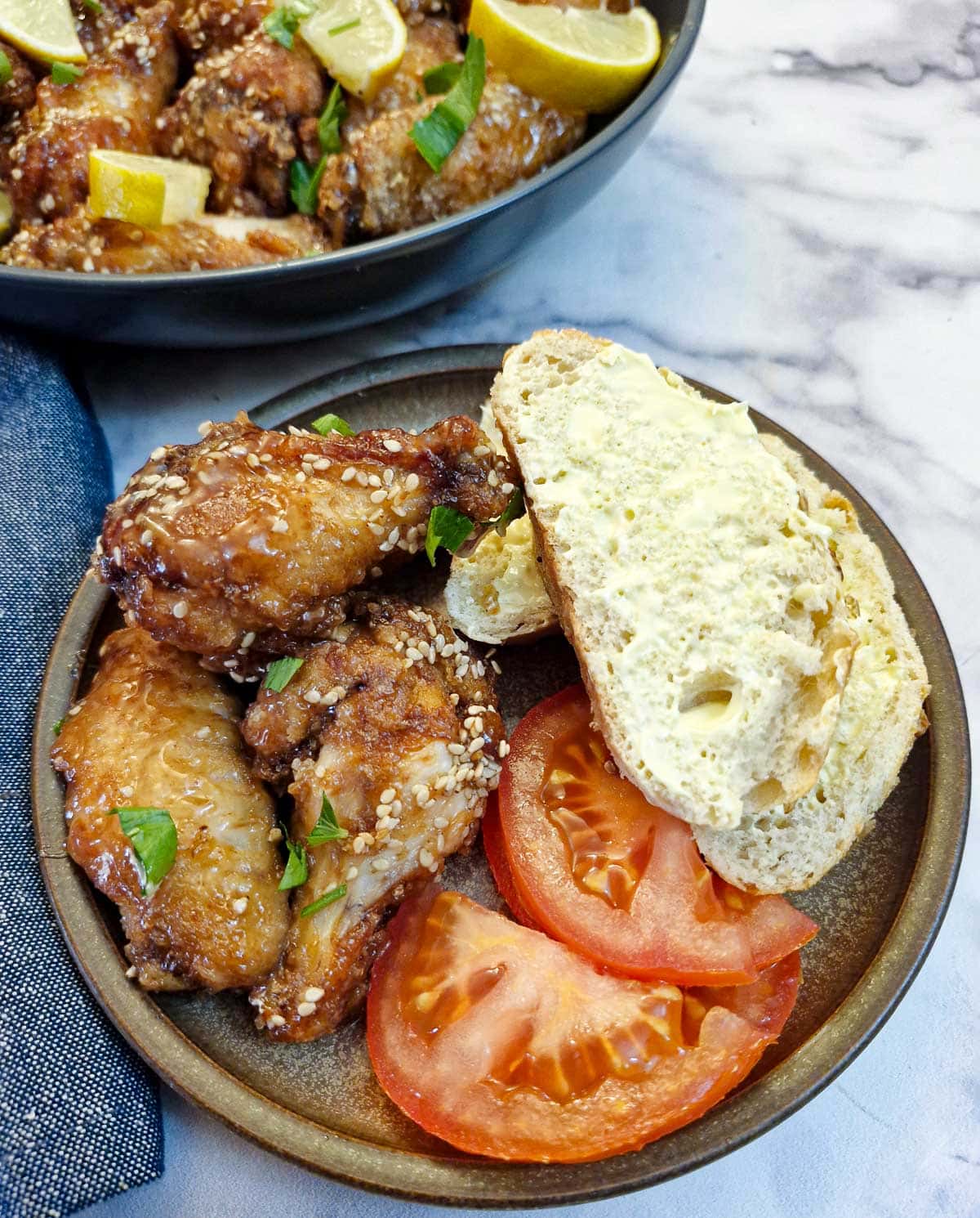 Three honey lemon chicken wings on a small brown plate with a slice of bread and 2 slices of tomato.
