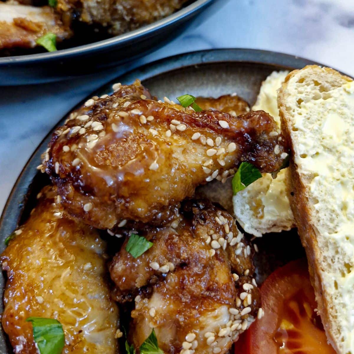 Three honey lemon chicken wings on a plate with a slice of crusty bread.