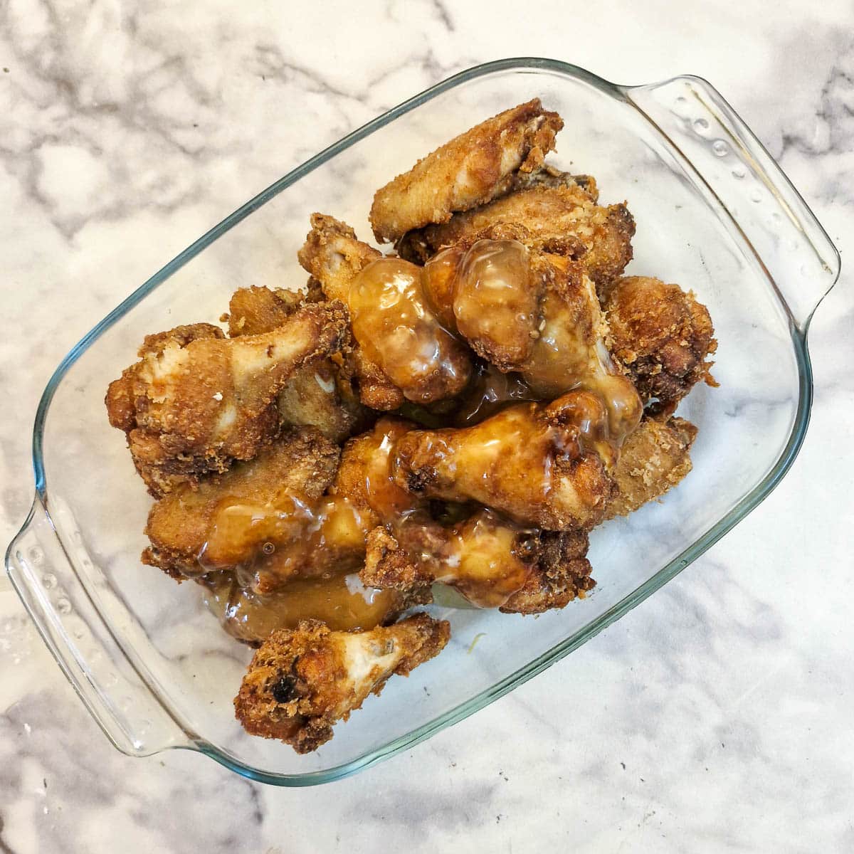 Chicken wings being coated with honey and lemon sauce in a glass bowl.
