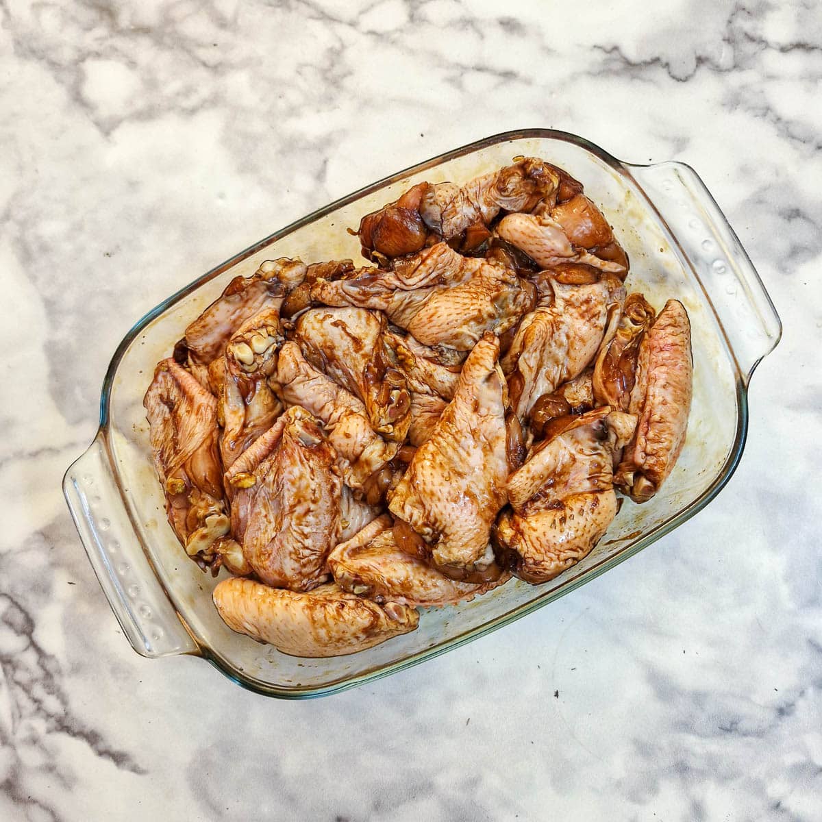 Chicken wings marinating in a glass dish.