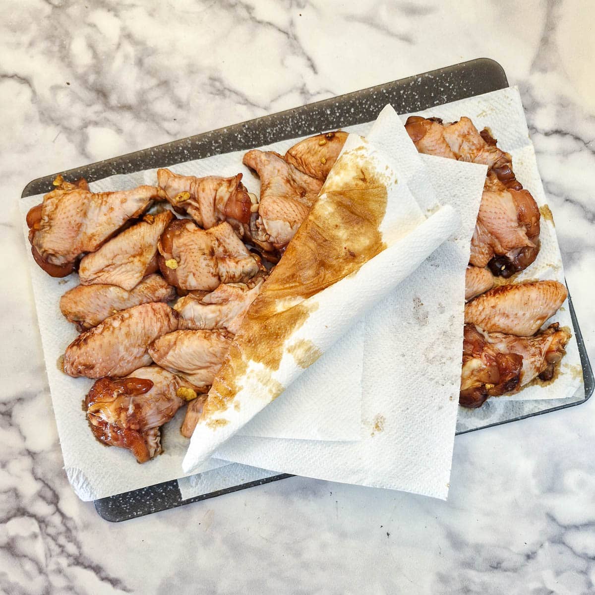 Chicken wings being patted dry with a paper towel.