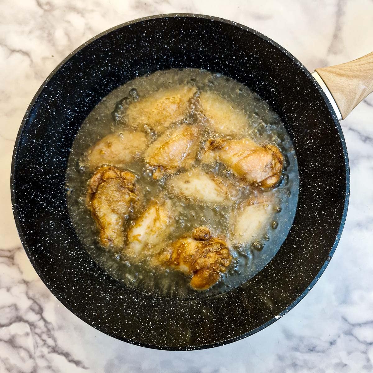 Chicken wings frying in oil in a wok.