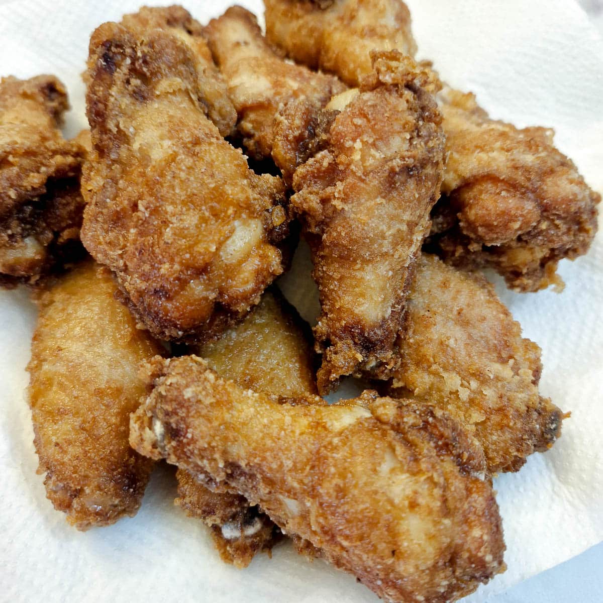 A pile of crispy chicken wings draining on a paper towel.