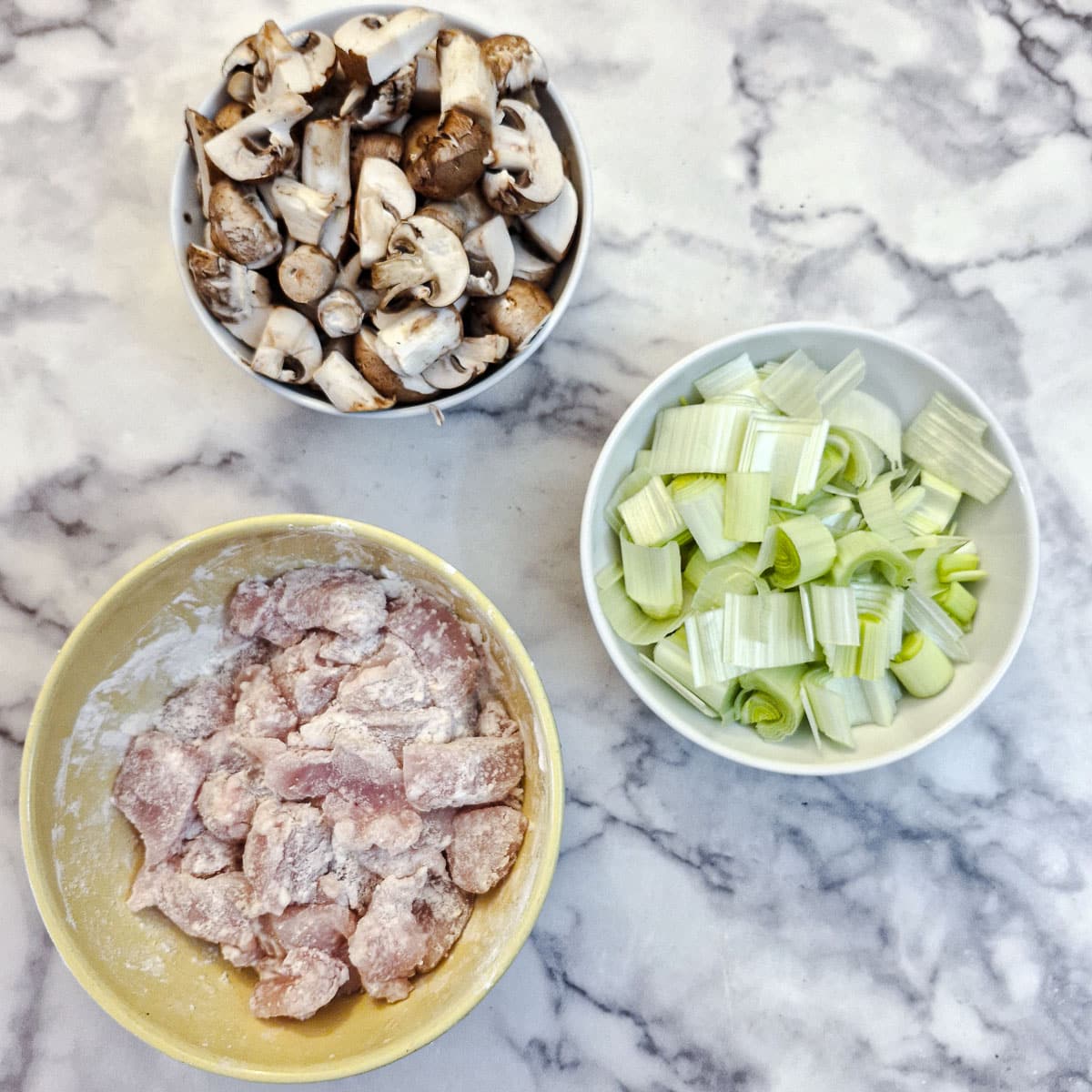 Three dishes of coated chicken, sliced mushrooms and chopped leeks.
