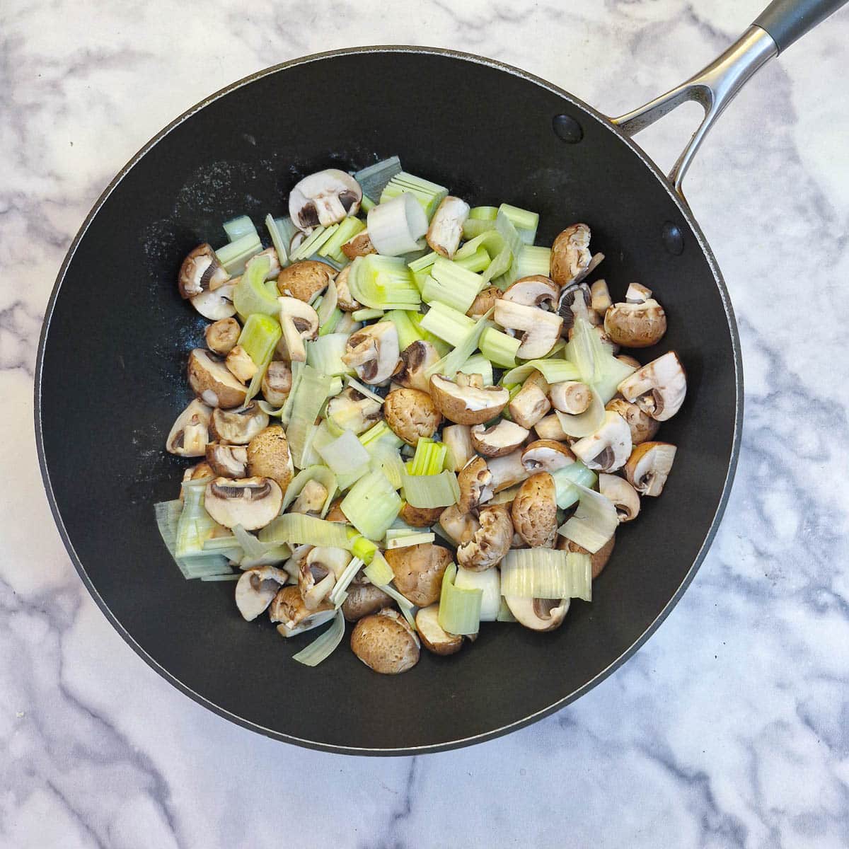 Mushrooms and leeks softening in butter in a frying pan.