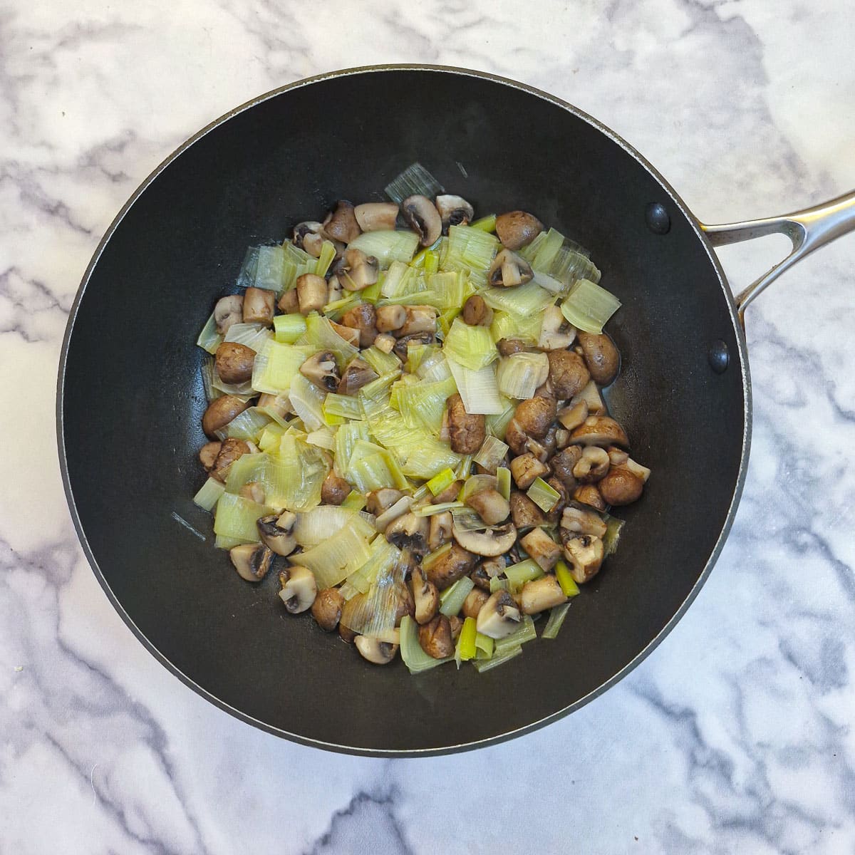 Cooked leeks and mushrooms in a frying pan.