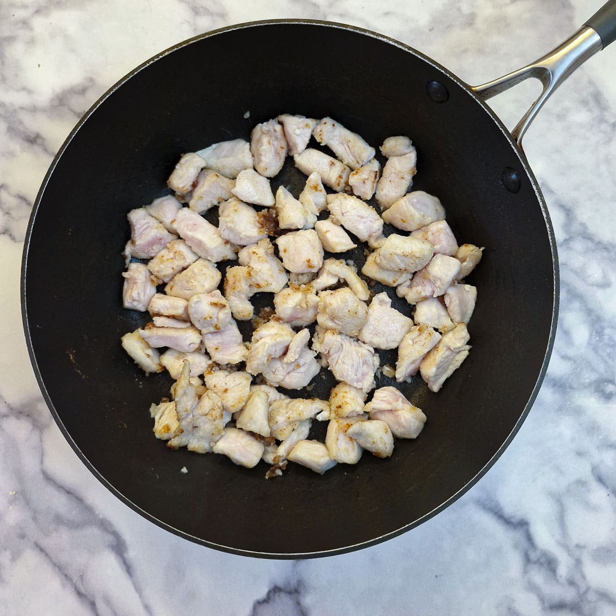 Chicken pieces browning in a frying pan.
