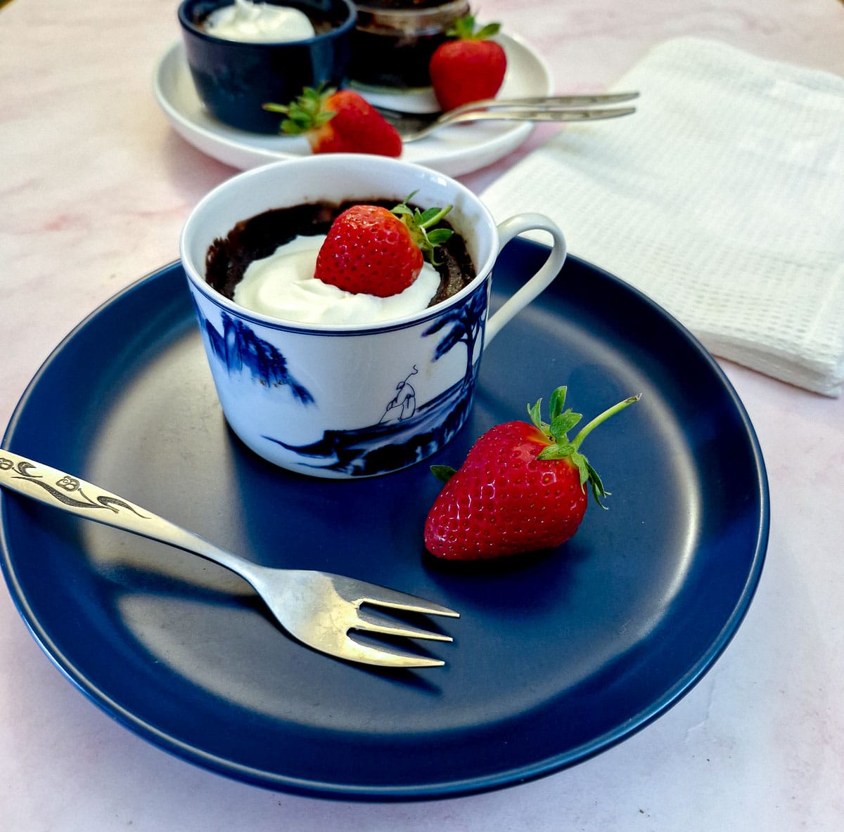 A microwave chocolate pot garnished with a strawberry in a blue and white cup on a blue plate.
