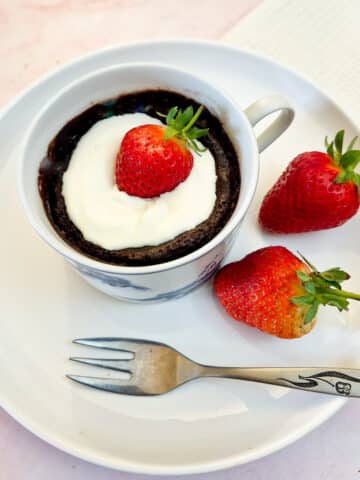 A microwave chocolate pot garnished with a strawberry in a white cup on a white plate.