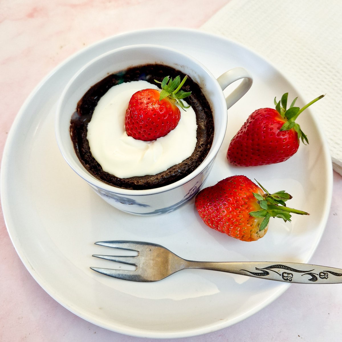 A microwave chocolate pot garnished with a strawberry in a white cup on a white plate.