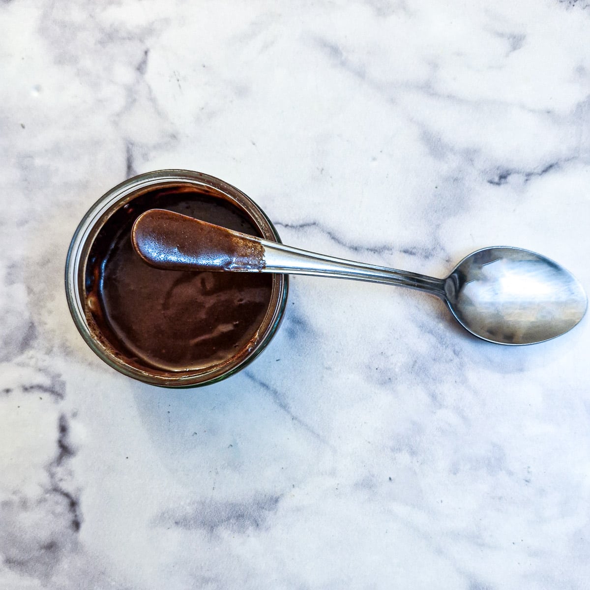 A chocolate pudding being mixed with the handle of a tablespoon.