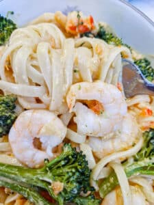 Sauce-coated linguine wrapped around a fork in a dish of prawn and broccoli pasta.