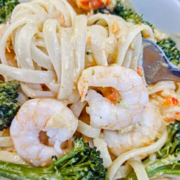 Sauce-coated linguine wrapped around a fork in a dish of prawn and broccoli pasta.