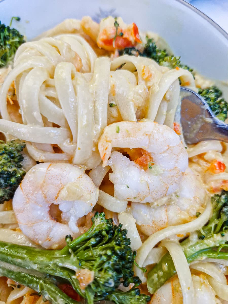 Sauce-coated linguine wrapped around a fork in a dish of prawn and broccoli pasta.