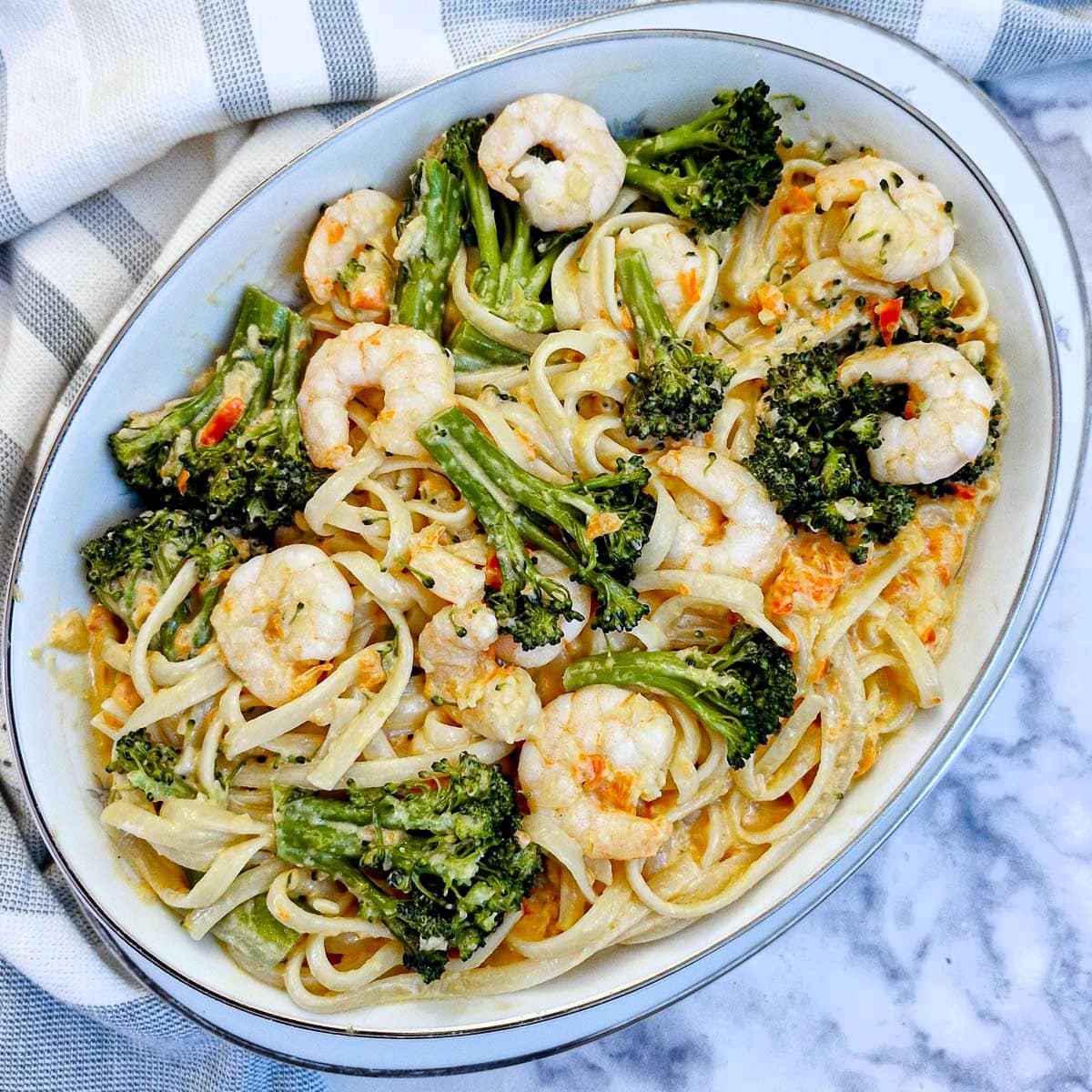 Overhead shot of a white serving dish filled with prawn and broccoli pasta.