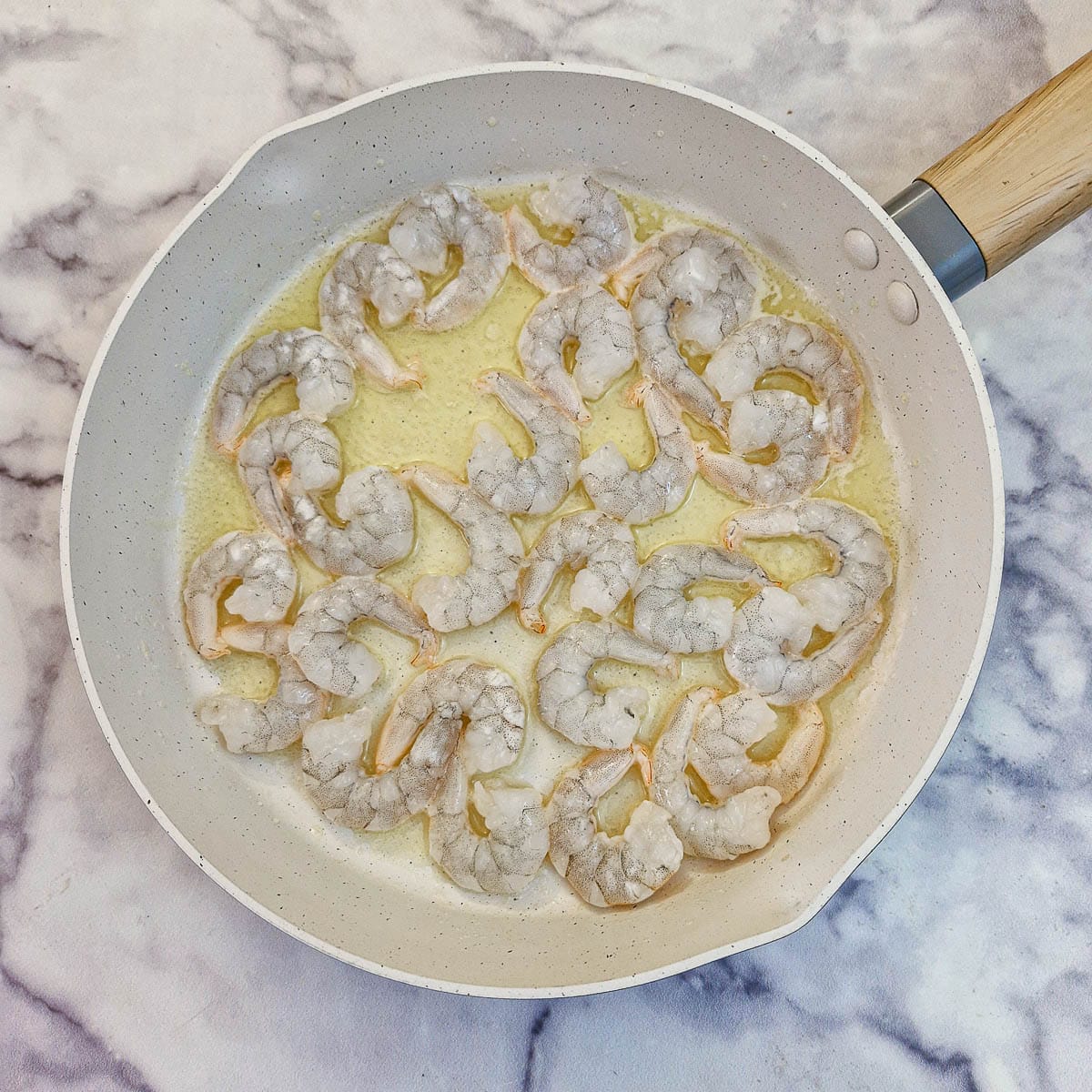 Raw prawns in melted butter in a frying pan.