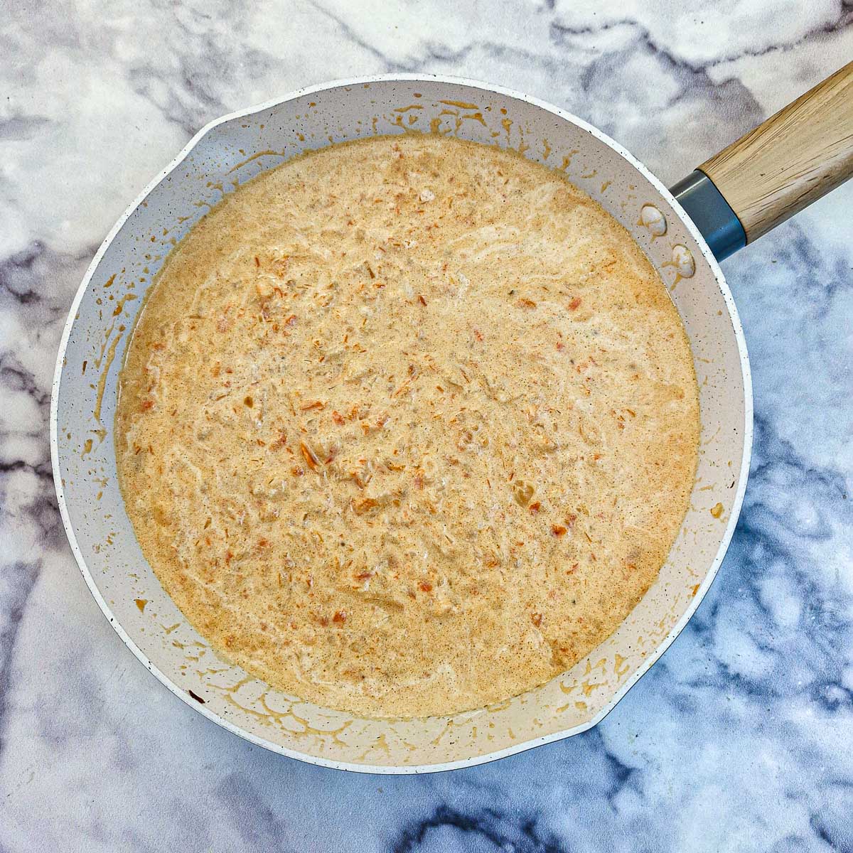 Cream stirred into the sauce in a frying pan.