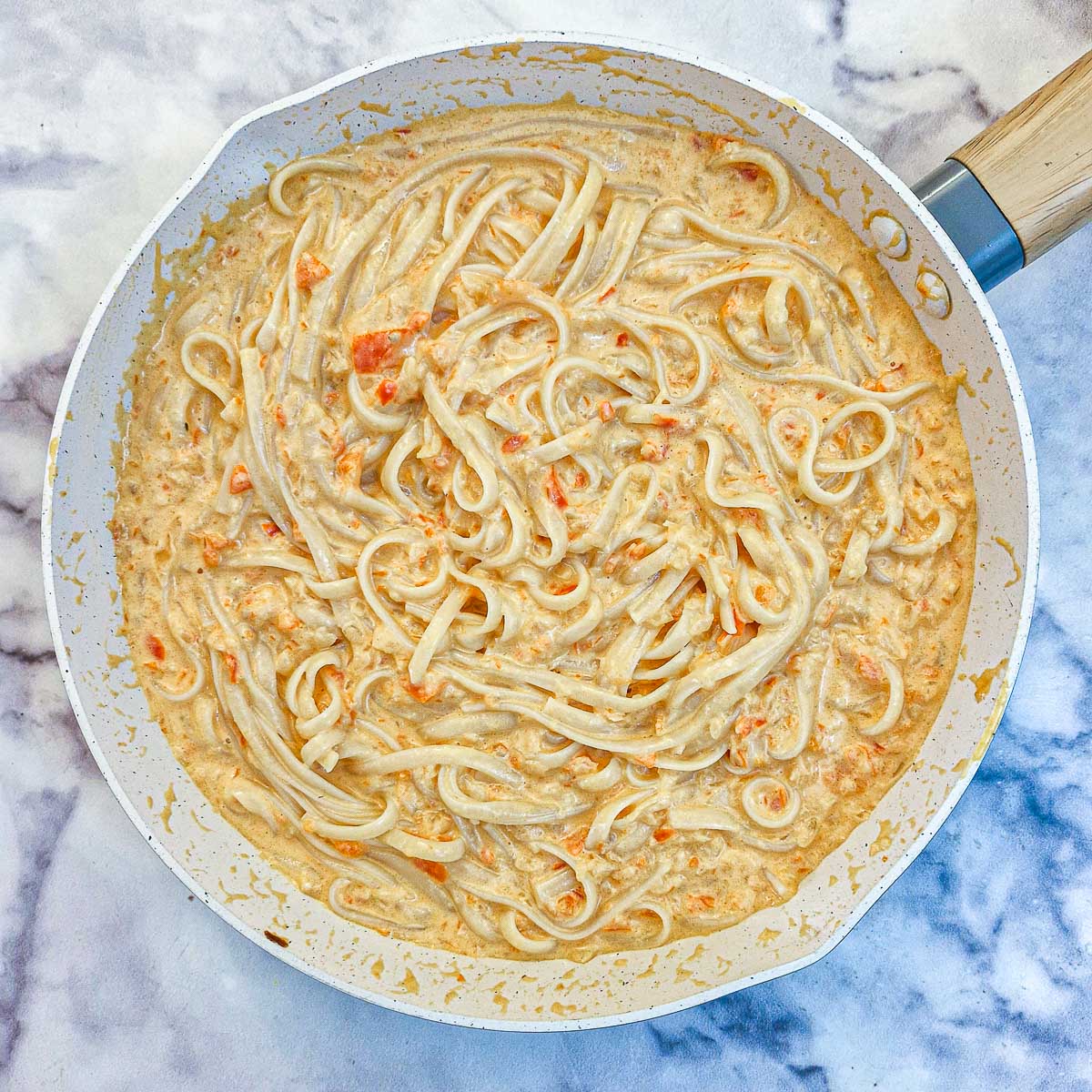 Linguine stirred into the red pepper sauce in a frying pan.