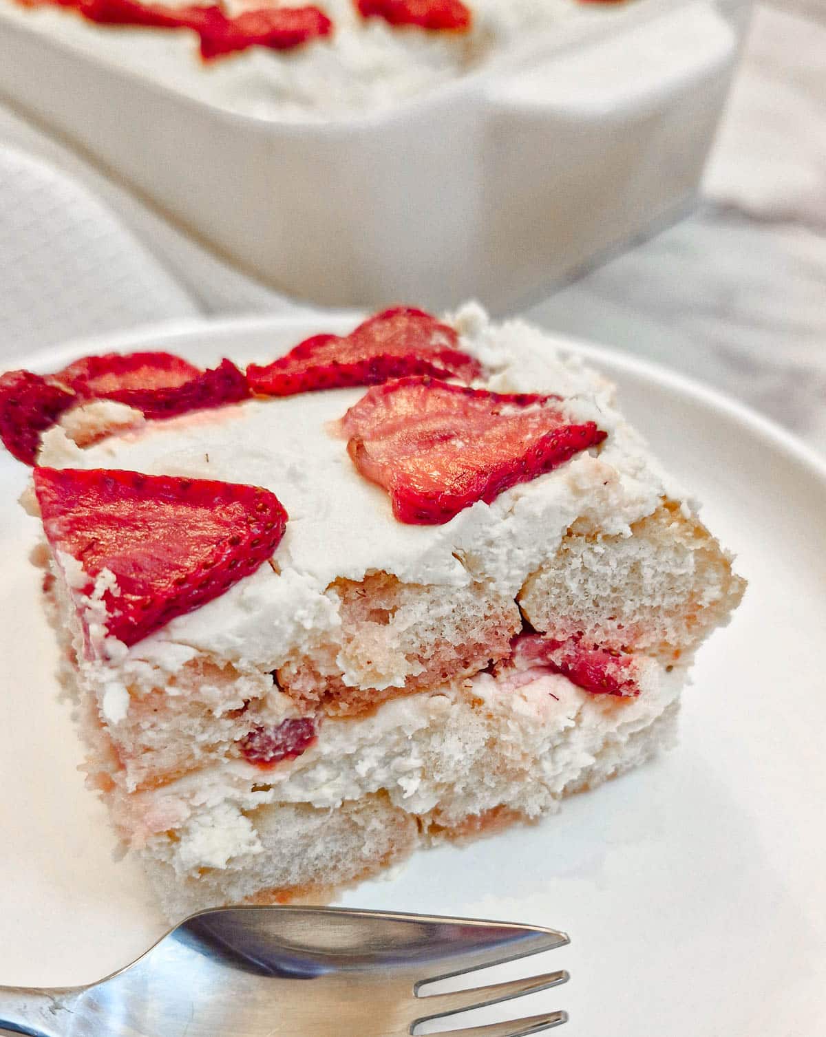 A slice of strawberry tiramisu on a white plate showing the layers of filling.