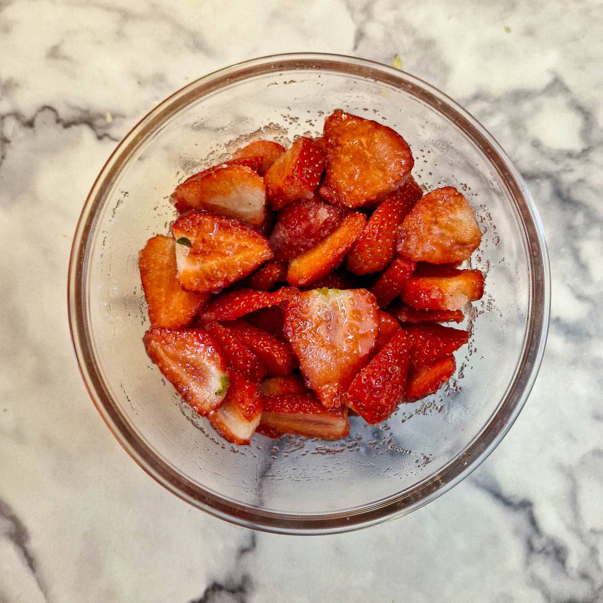 A glass bowl of sliced strawberries mixed with sugar.
