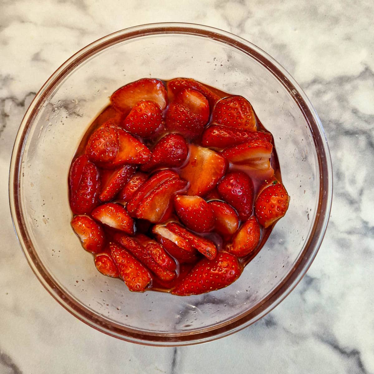 A glass bowl of strawberries showing the liquid that has been released to form a syrup.