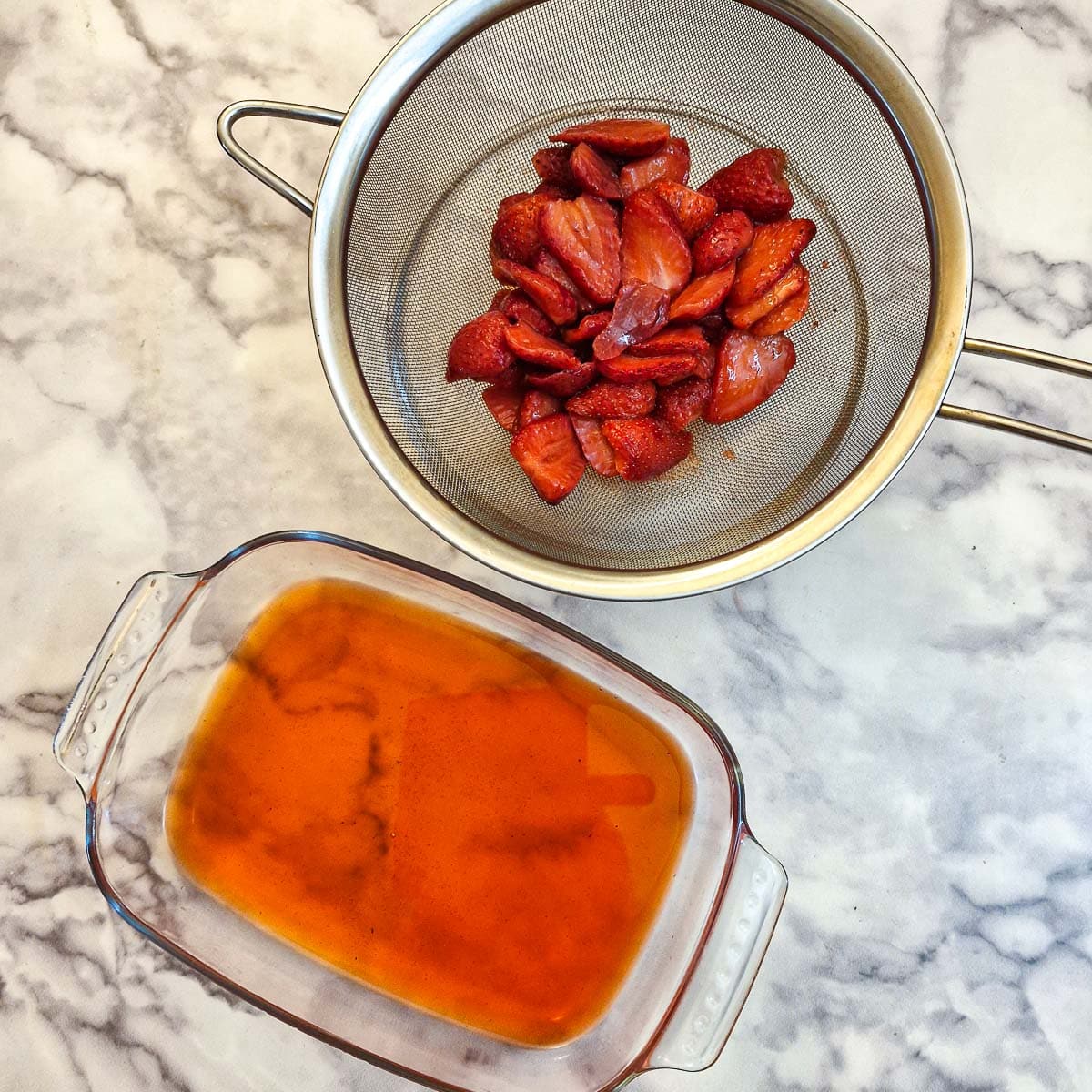 Strawberries in a sieve next to a dish of strawberry syrup.