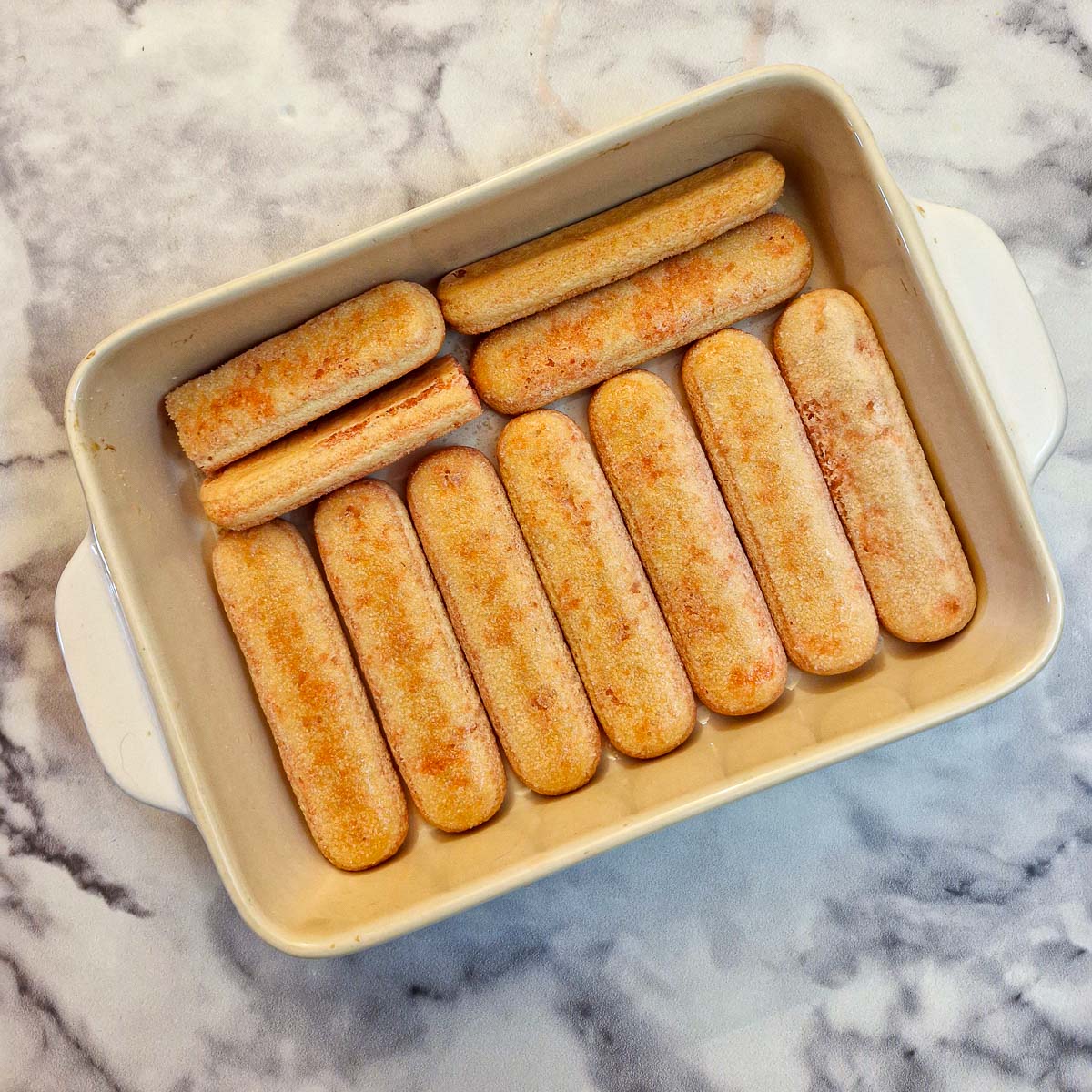 Sponge fingers dipped in strawberry syrup and arranged in a single layer in an oblong dish.