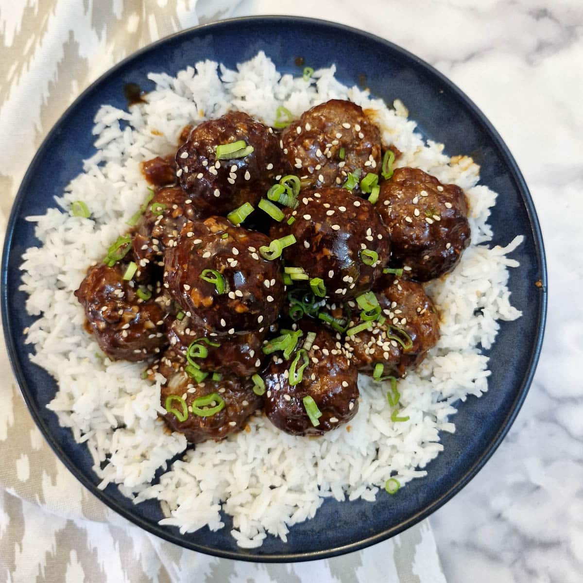 Sticky meatballs in teriyaki sauce on a bed of rice in a blue serving dish.