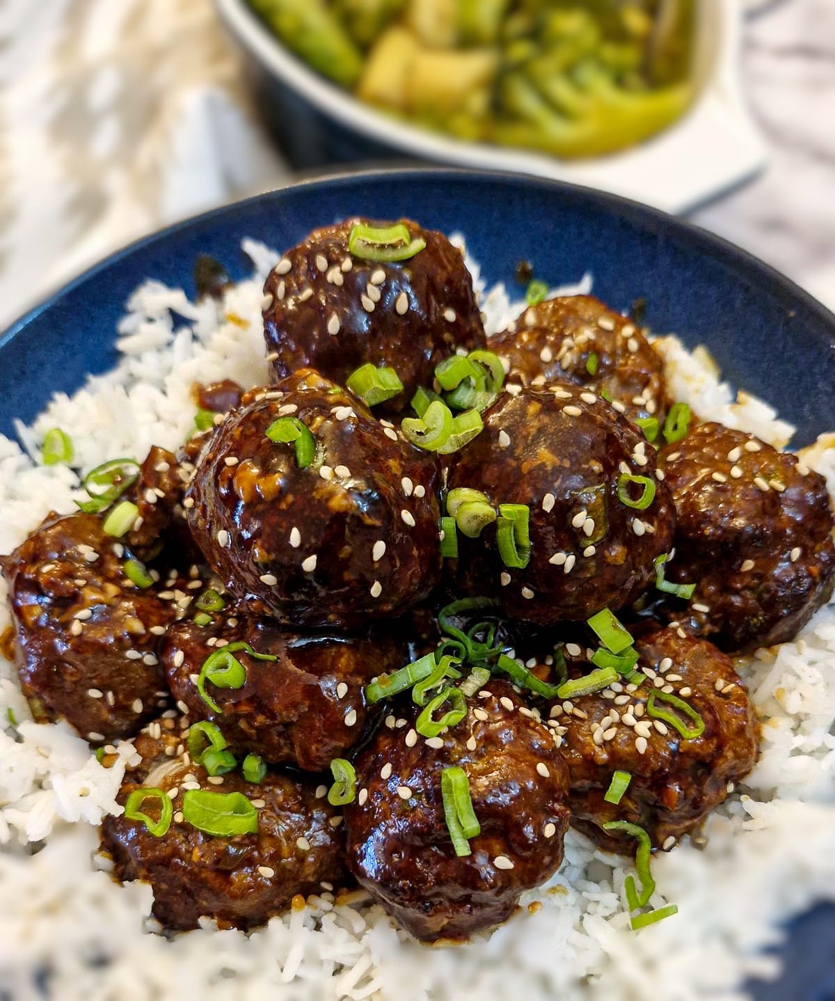 Close up of a dish of teriyaki meatballs on a bed of white rice in a serving dish.