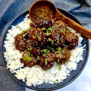 A pile of sticky teriyaki meatballs on a bed of rice in a blue serving dish.