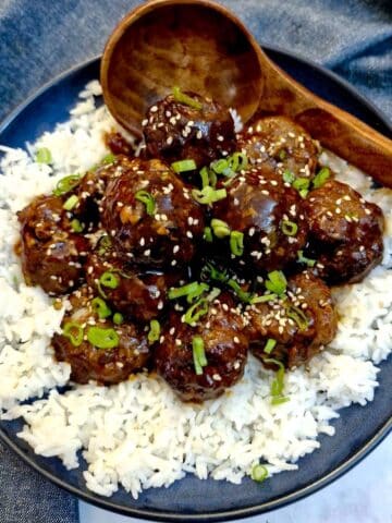 A pile of sticky teriyaki meatballs on a bed of rice in a blue serving dish.