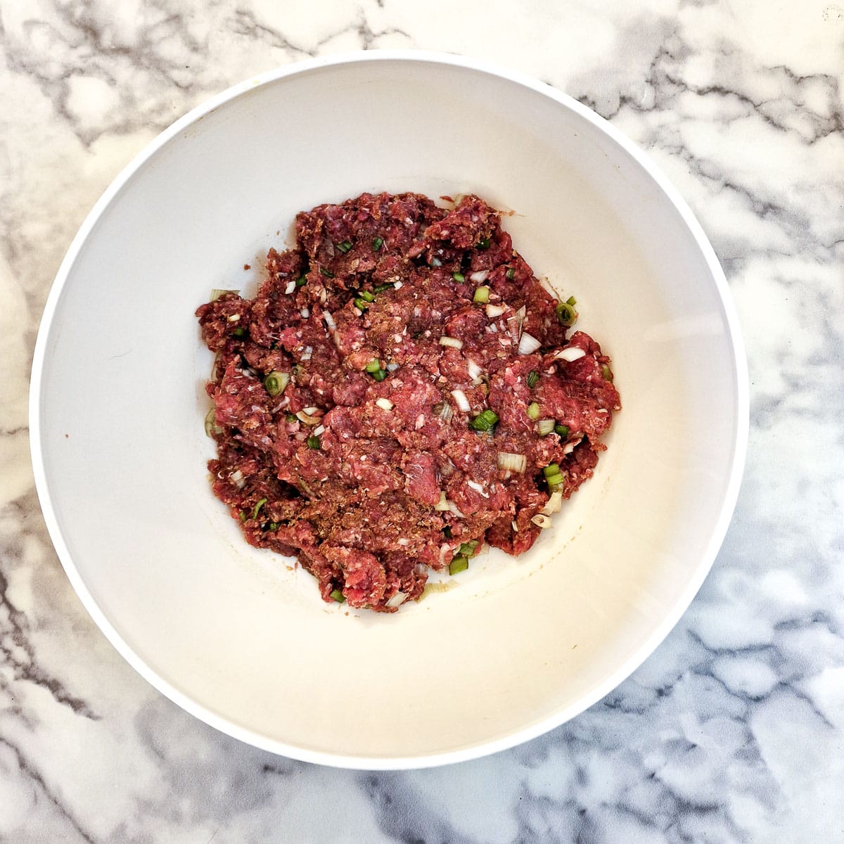 Meatball ingredients combined in a white mixing bowl.