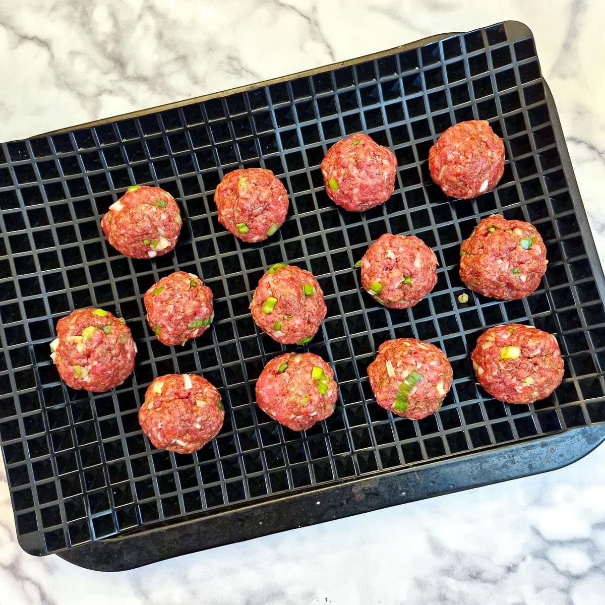 13 unbaked meatballs on a baking tray.