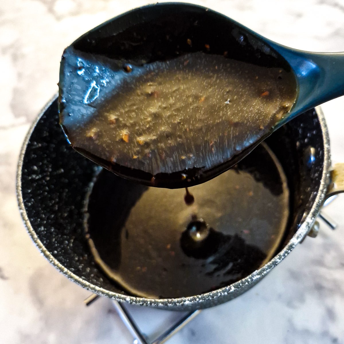 A spoonful of teriyaki sauce held over a saucepan showing the consistency of the the sauce.