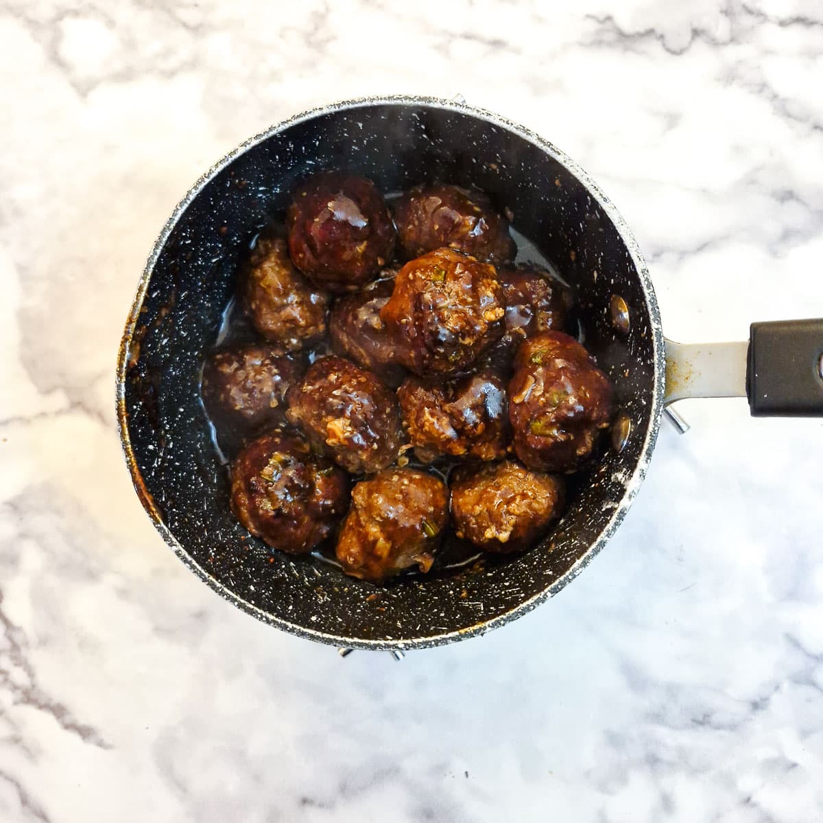 Meatballs combined with teriyaki sauce in a small saucepan.