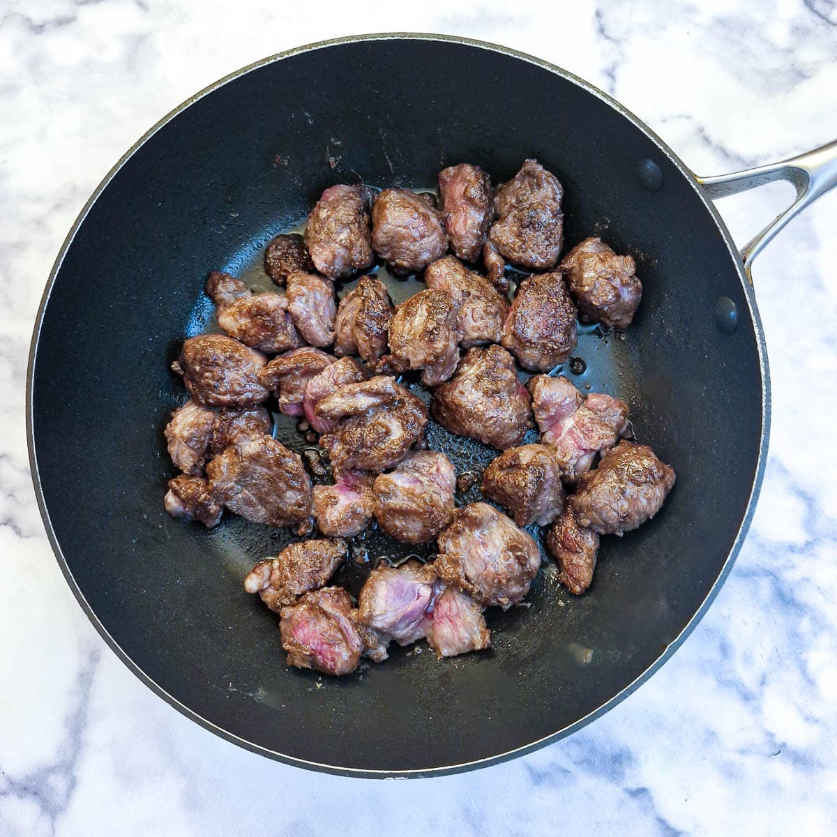 Cubes of lamb browning in a frying pan.
