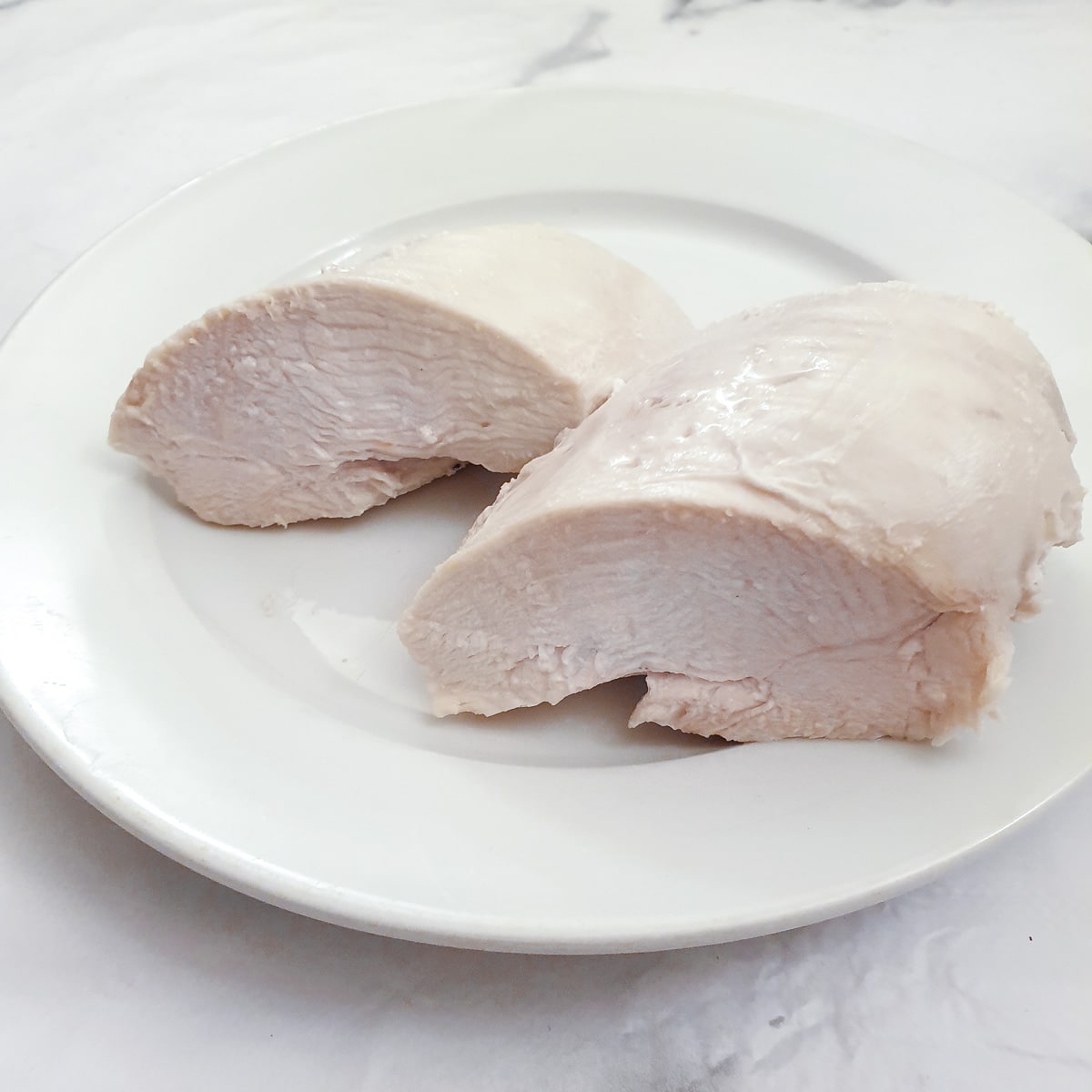 A poached chicken breast cut in half on a white plate.