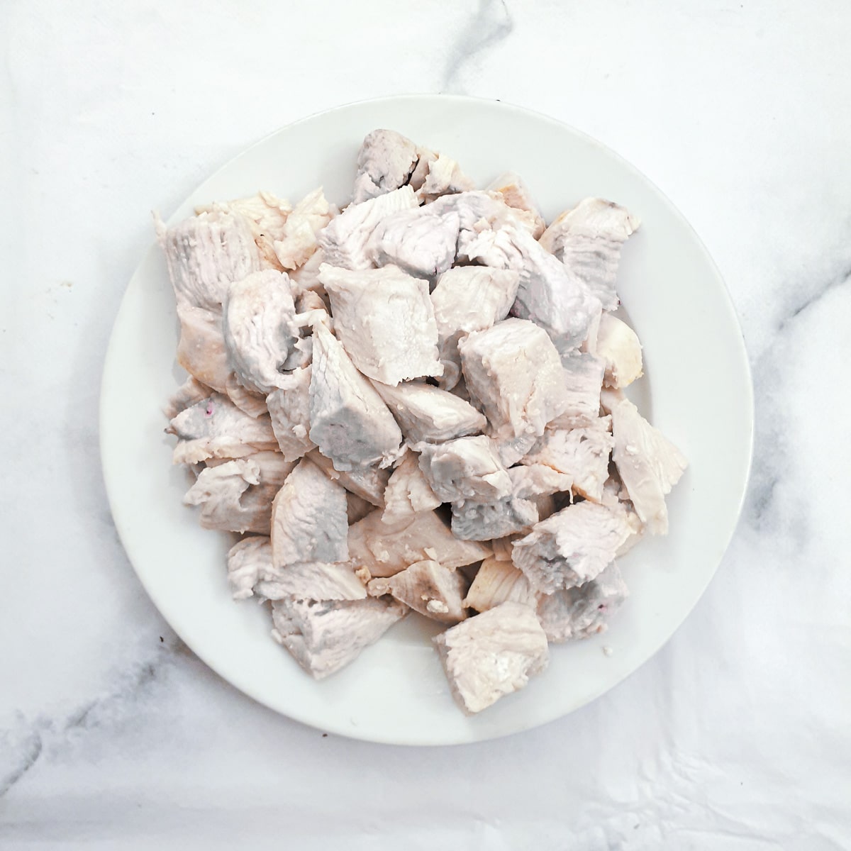 A pile of cooked chicken pieces on a white plate.