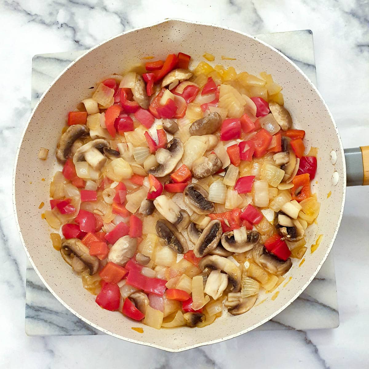 Red pepper, onions and mushrooms being sauteed in a frying pa.