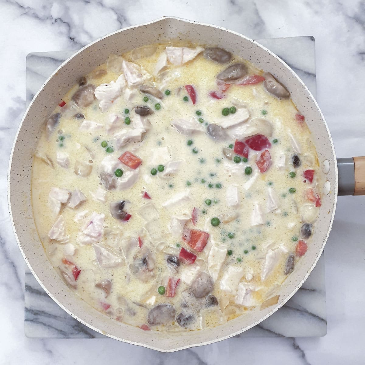 Peas and chicken added to the sauce in a frying pan.