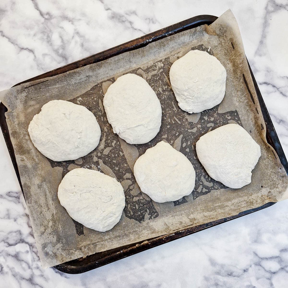 6 formed bread rolls on a baking sheet.