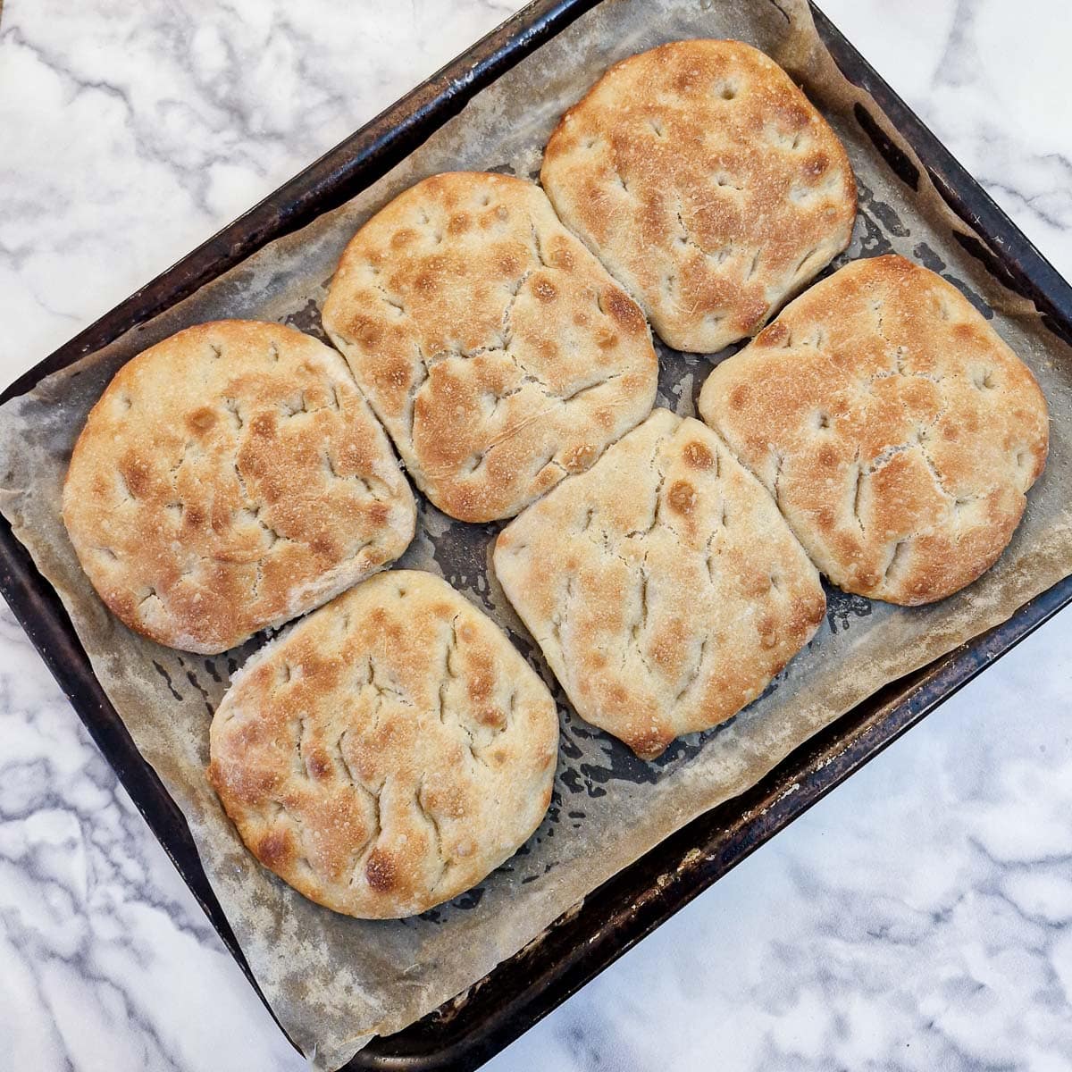 6 baked focaccia bread rolls on a baking tray.